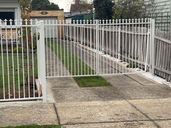 a white steel picket fence and gate beside a driveway
