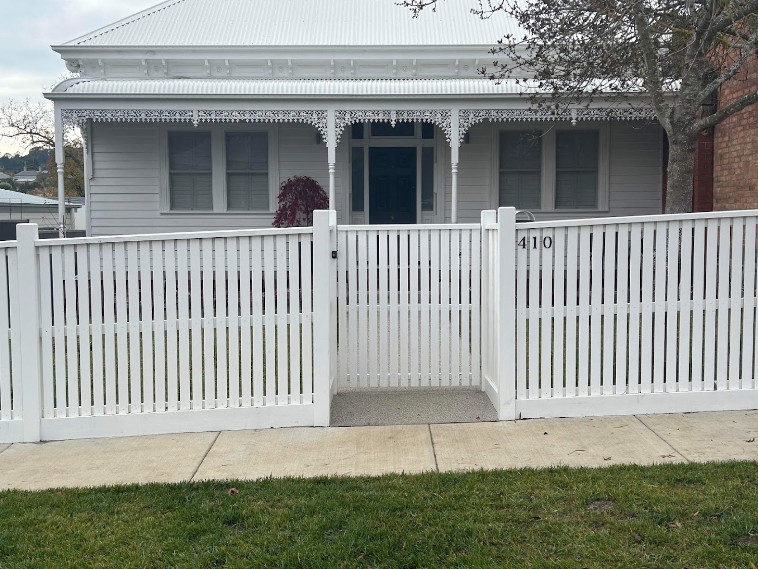 a white picket fence and gate in front of a weatherboard cottage