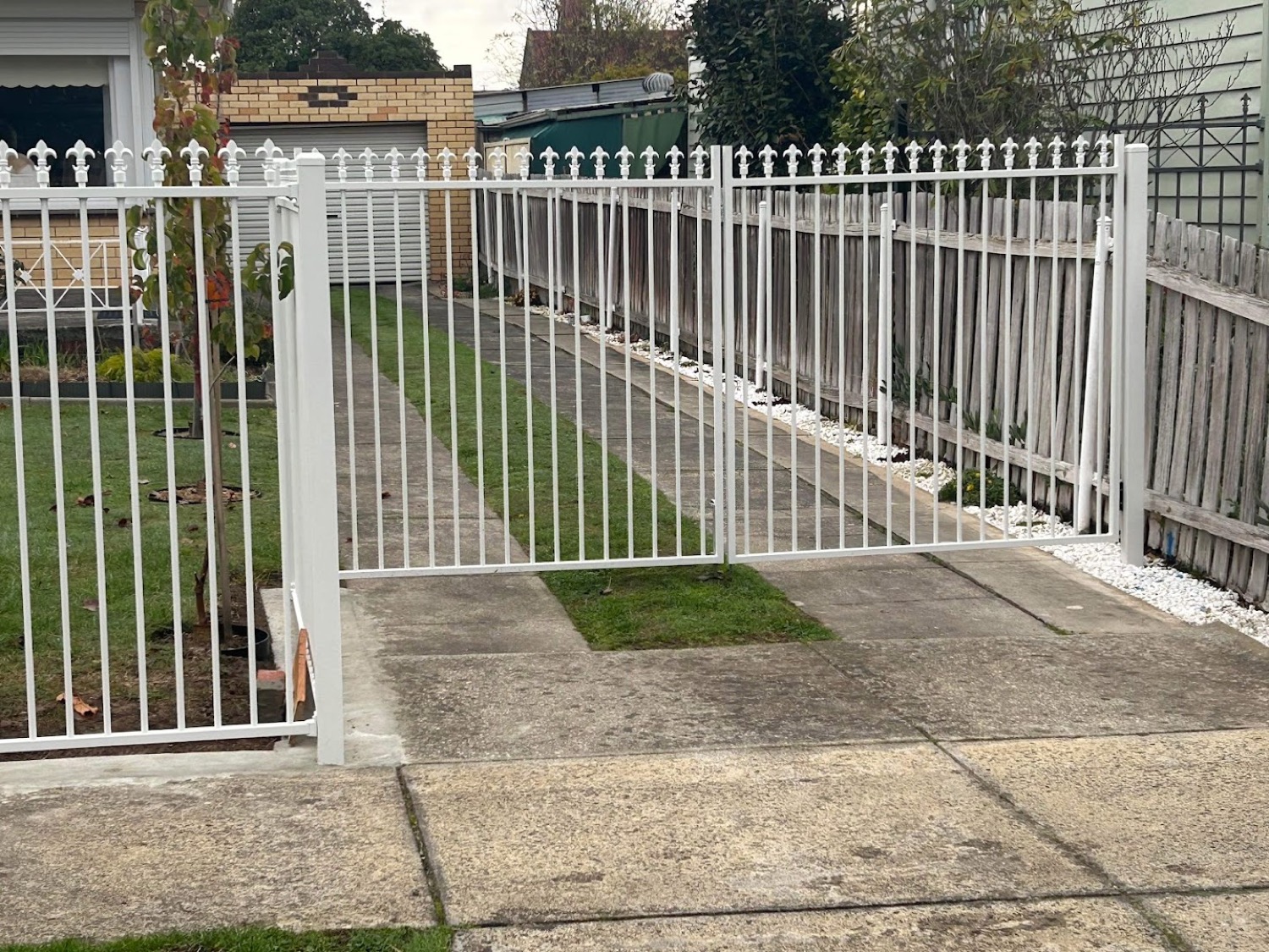 a white steel picket fence and gate beside a driveway