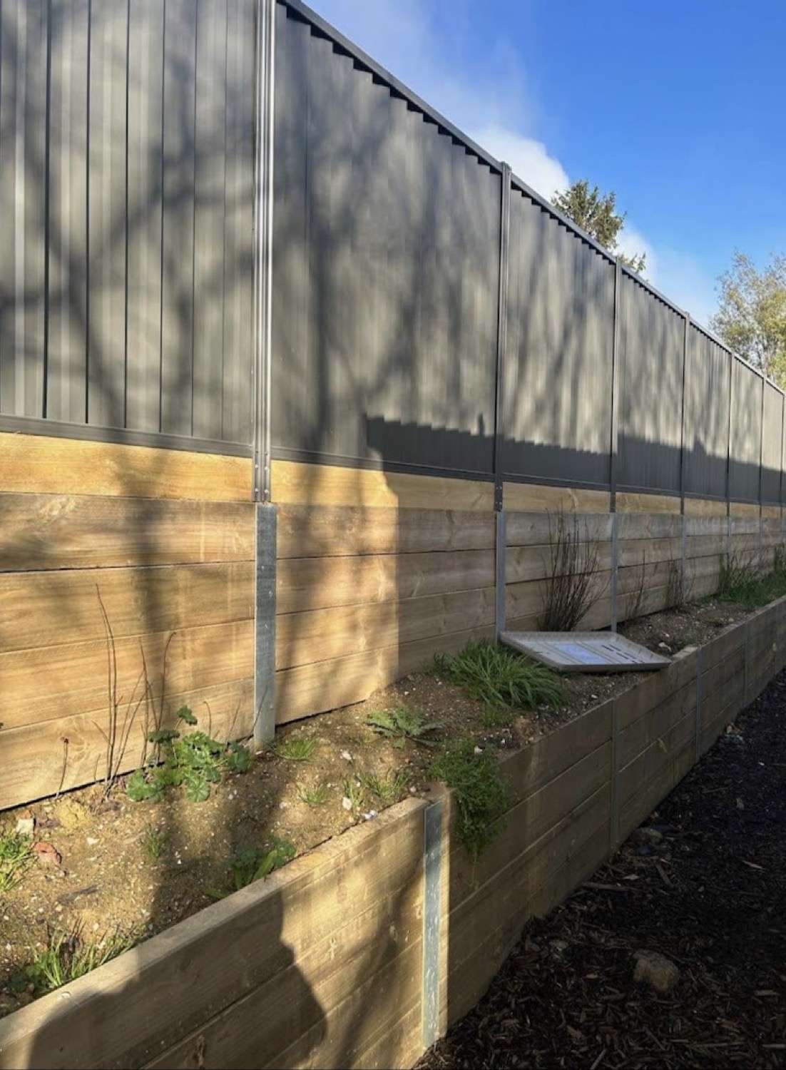 a Colorbond fence with a timber sleeper retaining wall below it