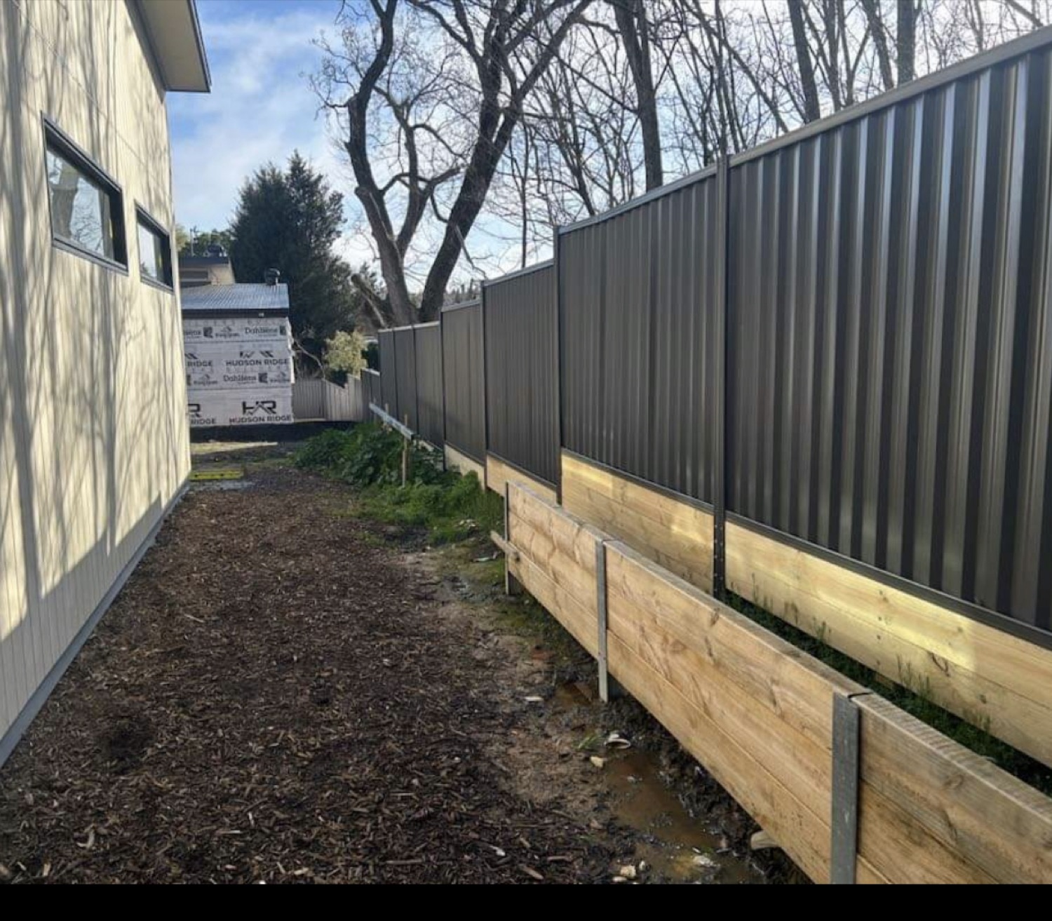 a Colorbond fence above timber sleepers beside a garden bed